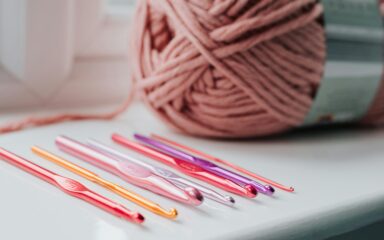 Close-up of colorful crochet hooks in vibrant pinks, purples, and orange, arranged on a white surface.