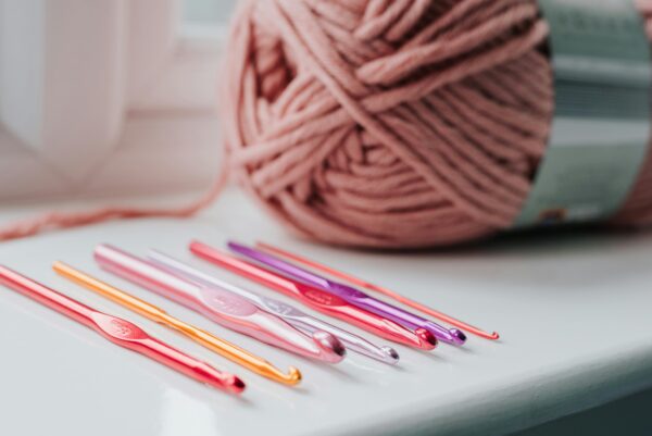 Close-up of colorful crochet hooks in vibrant pinks, purples, and orange, arranged on a white surface.